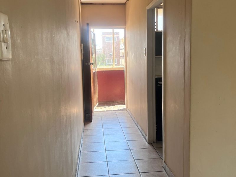 A narrow, empty hallway featuring ceramic floor tiles and neutral wall finishes, leading towards an exterior doorway.