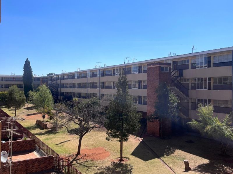 View of the apartment complex rear facade, featuring brick balconies, communal garden space, and external stairwell access.