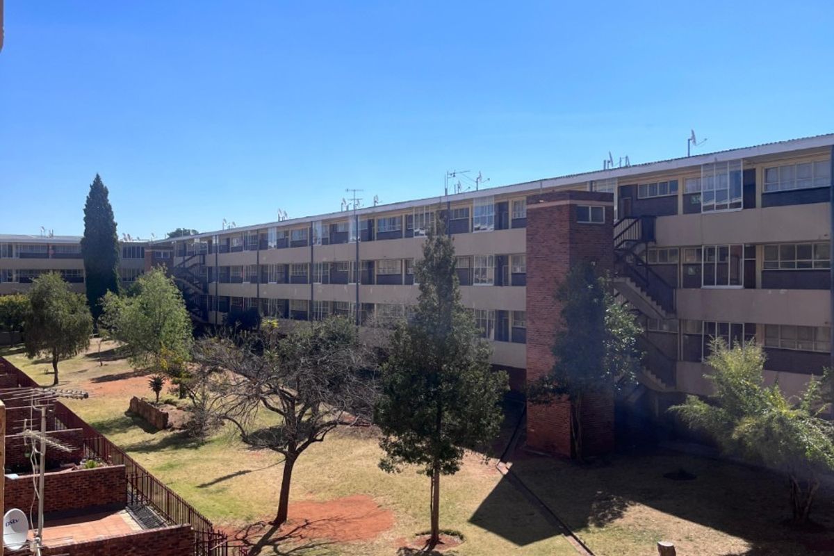 View of the apartment complex rear facade, featuring brick balconies, communal garden space, and external stairwell access.