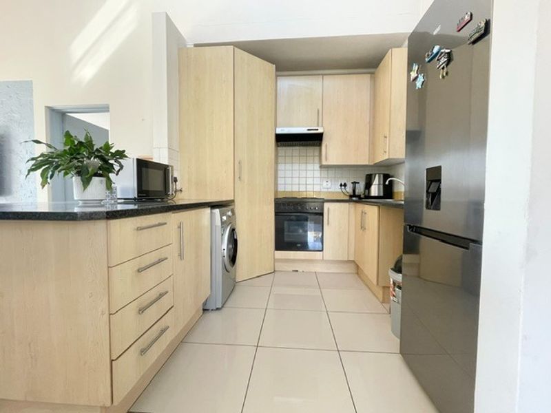 A functional kitchen featuring light wood cabinetry, dark countertops, tiled flooring, and built-in appliances including an oven and extractor fan.
