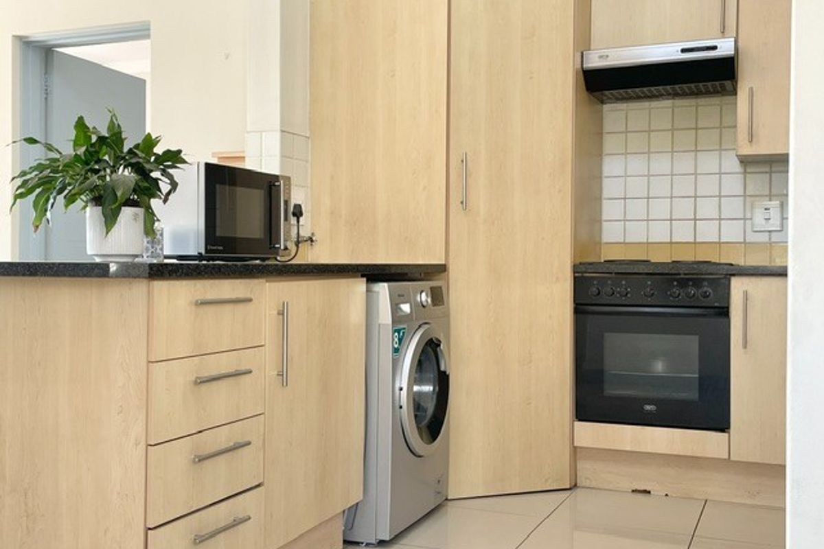 A functional kitchen featuring light wood cabinetry, granite countertops, a built-in oven with extractor fan, and tiled flooring.