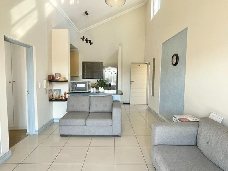 Open-plan living area featuring tiled flooring, vaulted ceilings, and a functional kitchen with a breakfast counter, creating a bright and spacious atmosphere.