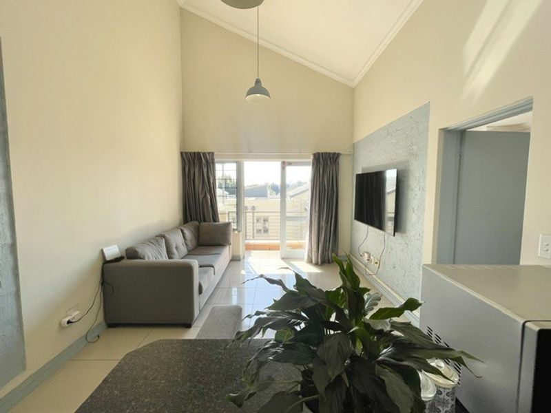 Open-plan living area featuring high vaulted ceilings, tiled floors, and a textured feature wall with direct access to a balcony.