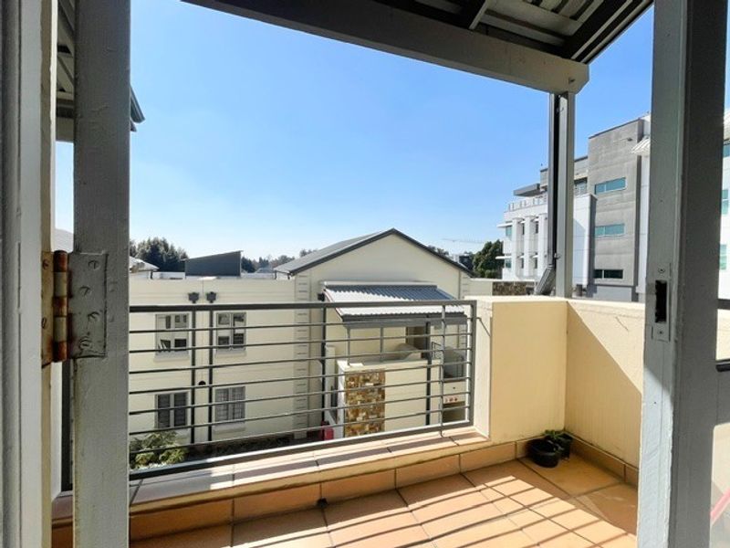 A private balcony featuring tiled flooring and a metal balustrade, offering an open view of the surrounding apartment complex.