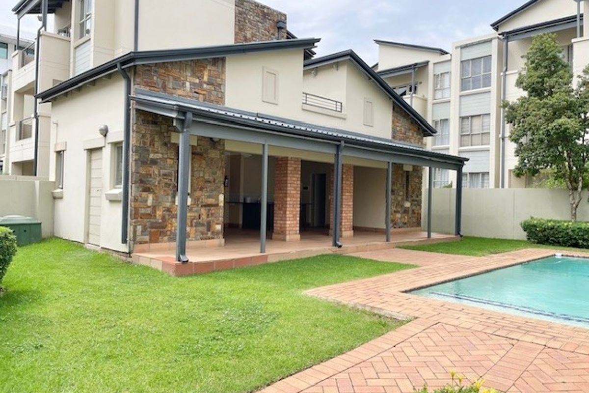 Rear view of the apartment featuring a covered patio with stone and brick accents, overlooking a private swimming pool and landscaped garden area.