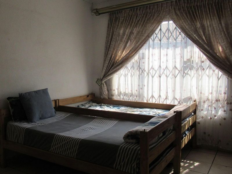 A bedroom featuring tiled flooring and a window fitted with a security gate and curtain rail.