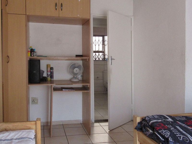 A bedroom featuring built-in cupboards and tiled flooring, with an adjacent bathroom visible through the open doorway.