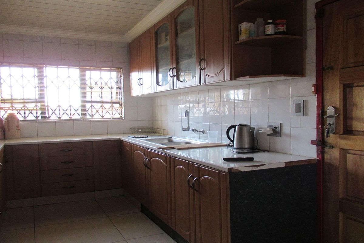 A functional kitchen featuring wooden cabinetry, tiled backsplash, and a stainless steel sink, with a window fitted with security bars.