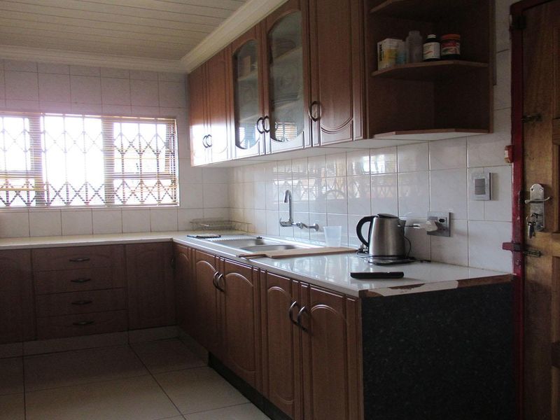 A functional kitchen featuring wooden cabinetry, tiled backsplash, and a stainless steel sink, with a window fitted with security bars.