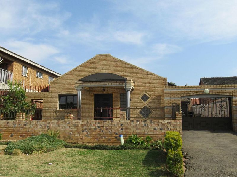 Front elevation of a face brick house featuring a paved driveway, secure wrought iron fencing, and a covered entrance porch.