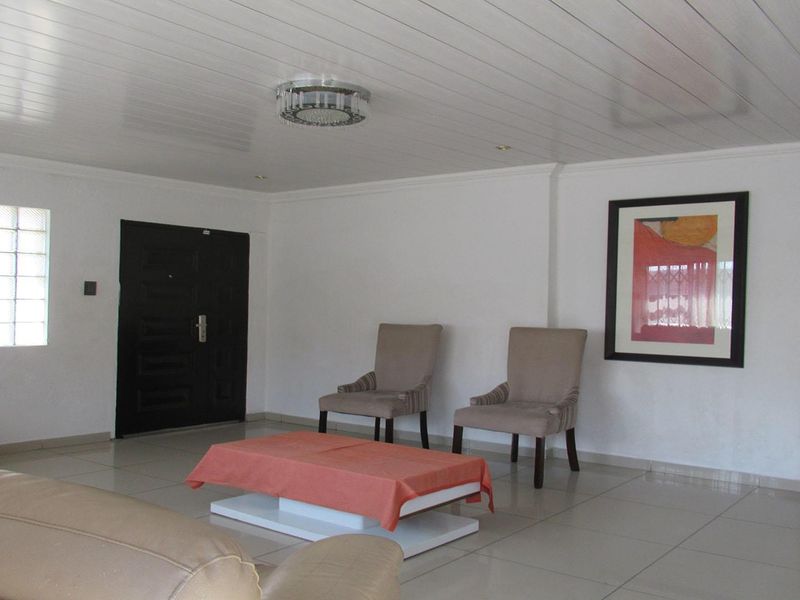 Spacious living area featuring neutral tiled flooring, a modern PVC panelled ceiling, and a distinctive glass block window for natural light.