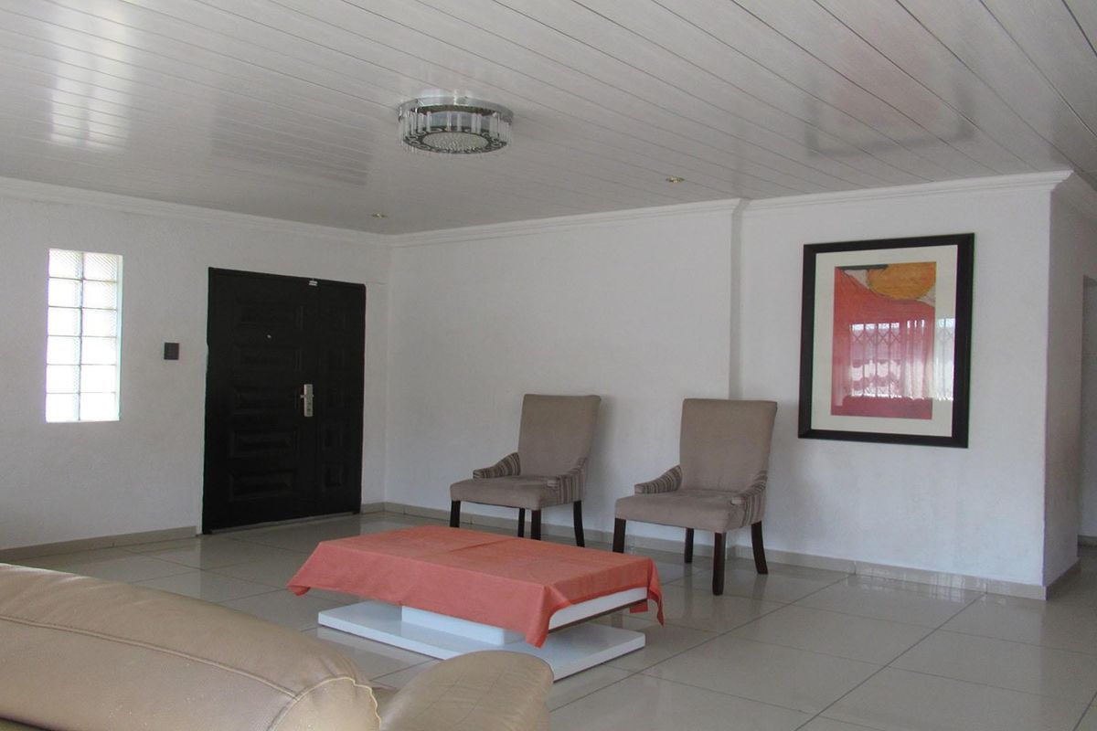 Spacious living area featuring neutral tiled flooring, a modern PVC panelled ceiling, and a distinctive glass block window for natural light.