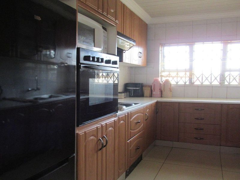 A functional kitchen featuring wooden cabinetry, built-in oven, extractor fan, tiled backsplash, and tiled flooring with natural light from the window.