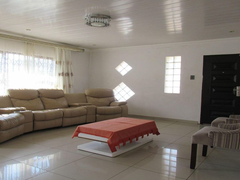 Spacious living room featuring tiled flooring, glossy ceiling panels, and unique diamond-shaped feature windows, offering a bright and open atmosphere.
