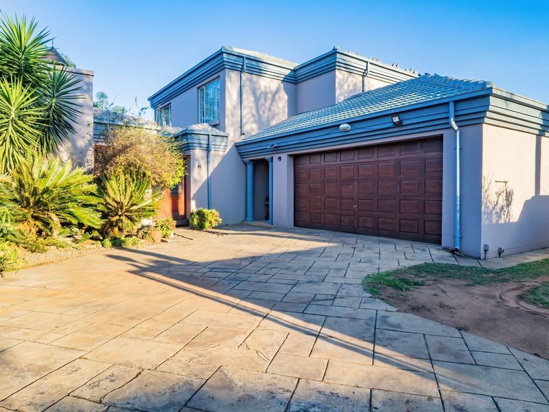 Front elevation of a double-story house featuring a paved driveway, integrated double garage, and established garden landscaping.
