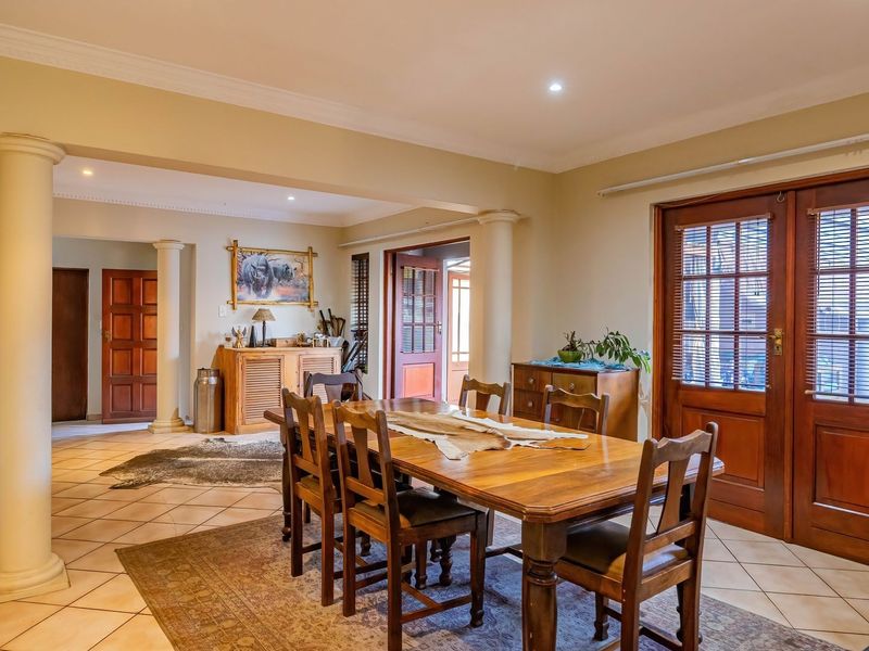 Spacious dining area featuring classic tiled flooring, decorative columns, and wooden french doors that provide natural light and access to the exterior.
