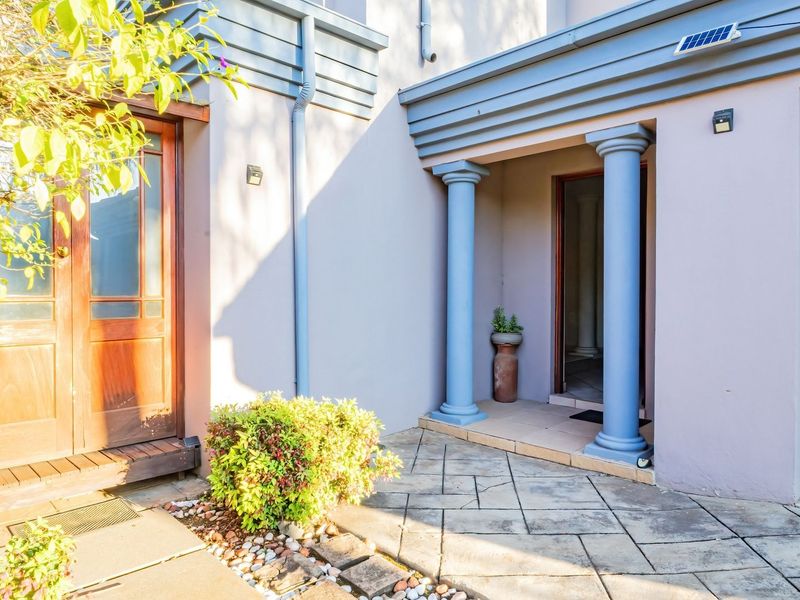 Front entrance area featuring a wooden double door, decorative columns, and paved patio space leading to the main residence and garage.