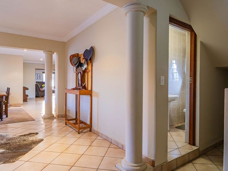 Spacious hallway featuring decorative columns, ceramic tile flooring, and crown molding, with direct access to a small guest bathroom.