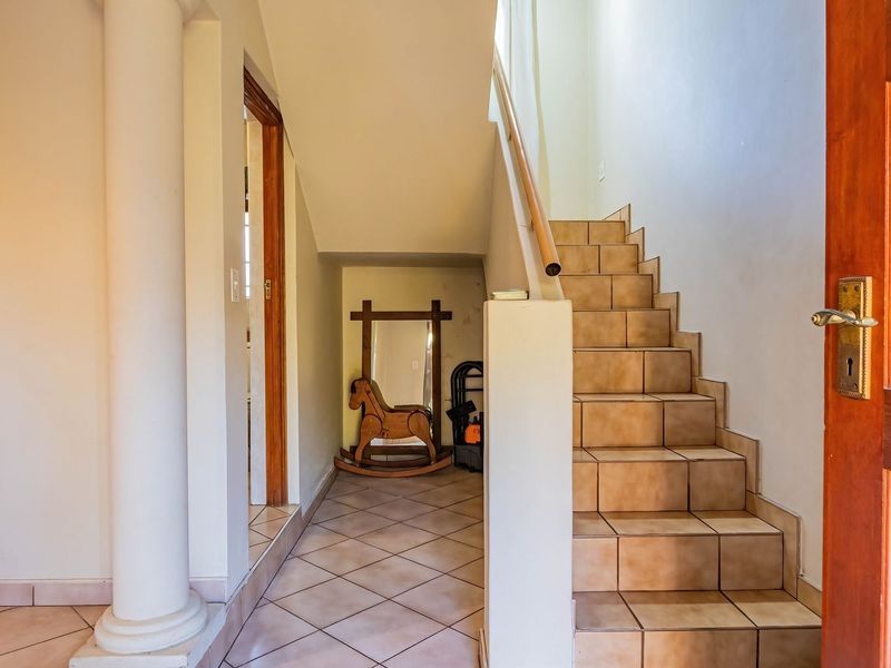 A tiled hallway featuring a staircase with a wooden handrail and a decorative column, leading to an adjacent room.