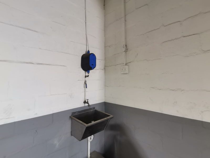 A functional utility area featuring a stainless steel sink, wall-mounted dispenser, and exposed electrical and plumbing infrastructure.