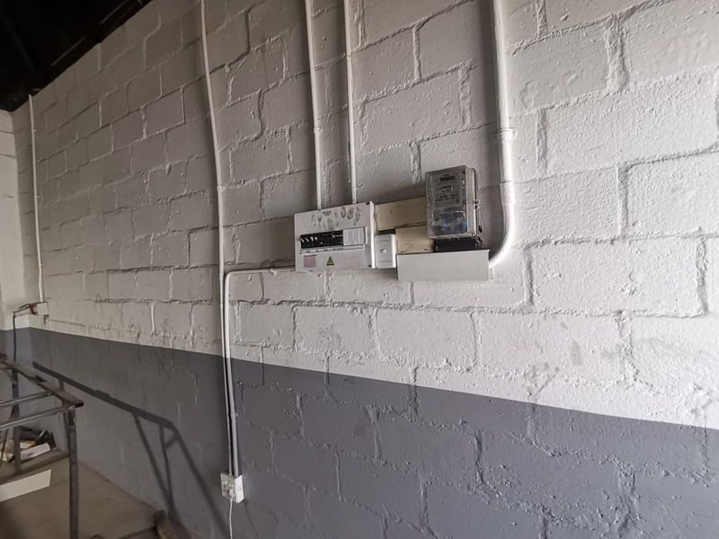 Industrial utility space featuring a wall-mounted electrical distribution board and electricity meter with exposed conduit on painted concrete block walls.