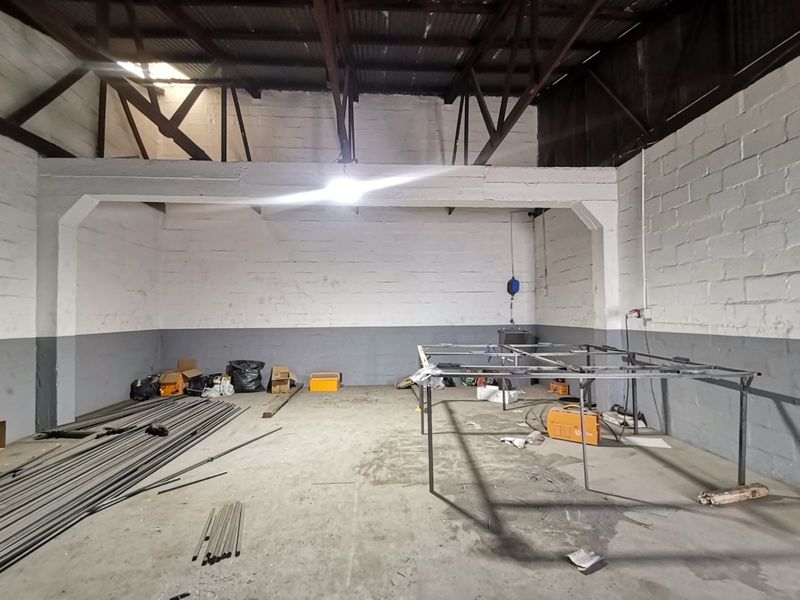 Industrial utility space featuring exposed steel roof trusses, concrete block walls, and durable concrete flooring, suitable for workshop or storage use.