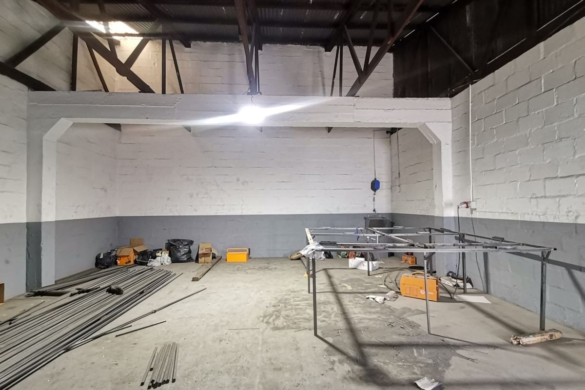 Industrial utility space featuring exposed steel roof trusses, concrete block walls, and durable concrete flooring, suitable for workshop or storage use.
