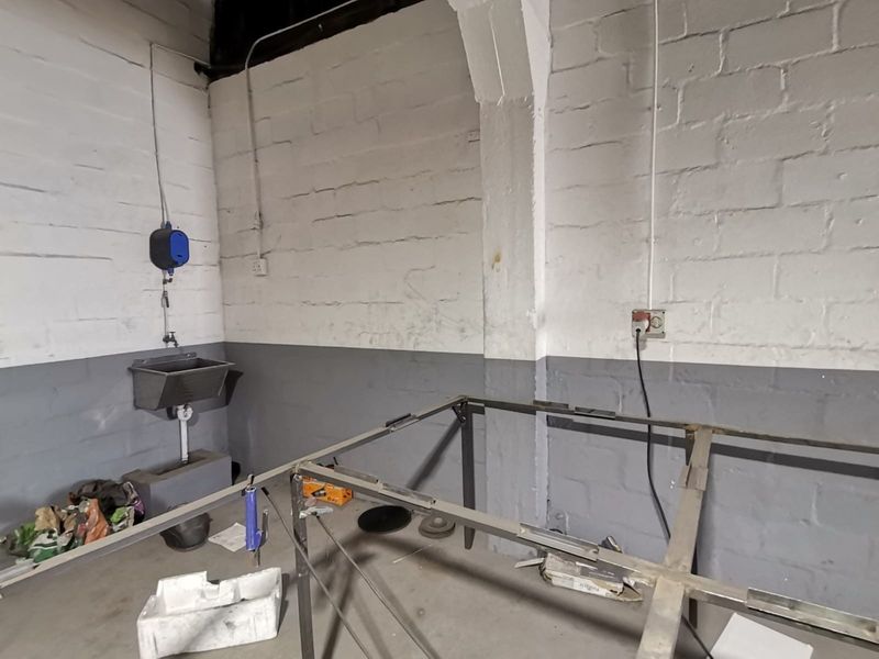 Industrial utility space featuring exposed brick walls, concrete flooring, and a wall-mounted utility sink with exposed plumbing and electrical conduits.