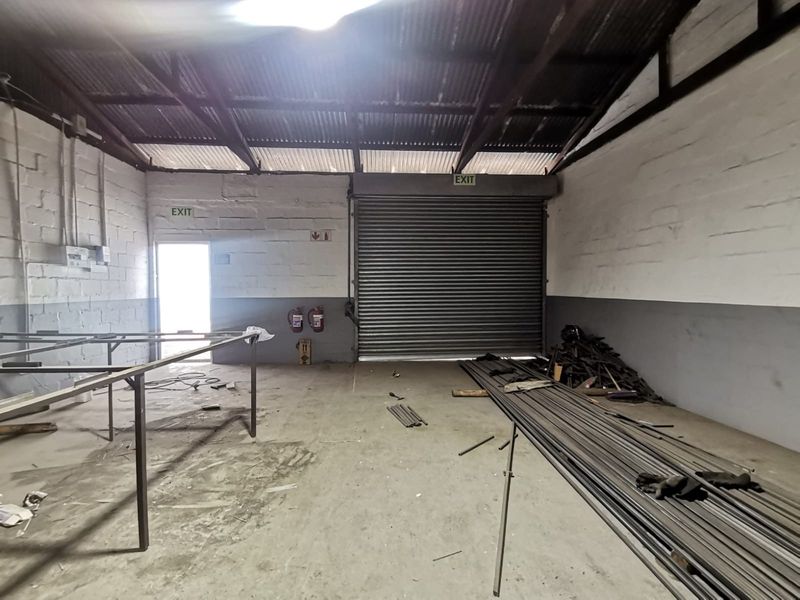 Industrial utility space featuring a large roller shutter door, exposed steel roof trusses, and functional fire safety equipment, suitable for workshop or storage use.