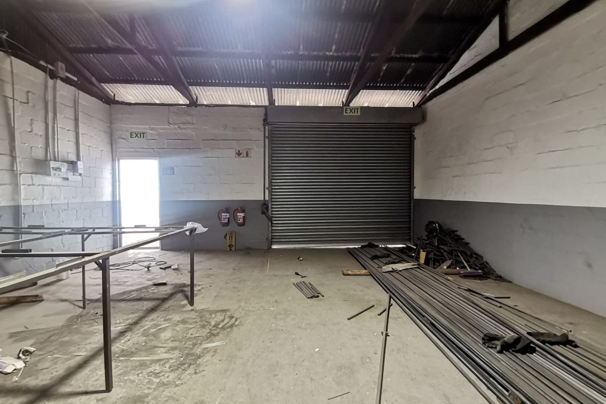 Industrial utility space featuring a large roller shutter door, exposed steel roof trusses, and functional fire safety equipment, suitable for workshop or storage use.