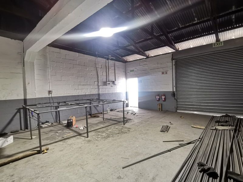 Spacious industrial utility area featuring high ceilings with exposed steel trusses, a large roller shutter door, and durable concrete block walls.