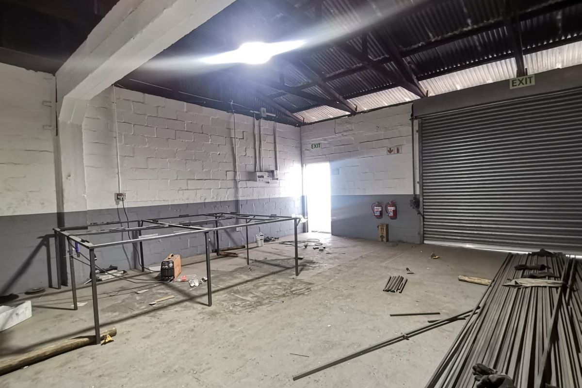 Spacious industrial utility area featuring high ceilings with exposed steel trusses, a large roller shutter door, and durable concrete block walls.