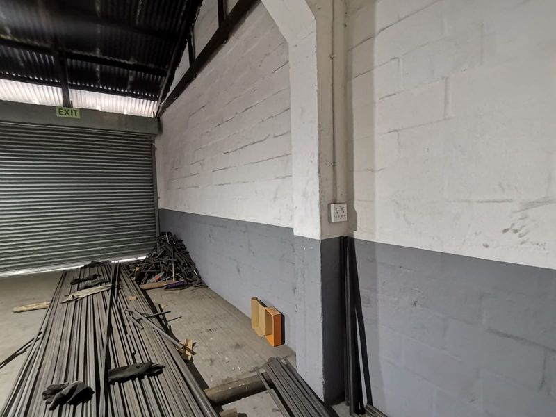 Industrial utility space featuring high ceilings with exposed trusses, a large roller shutter door, and durable painted masonry walls.
