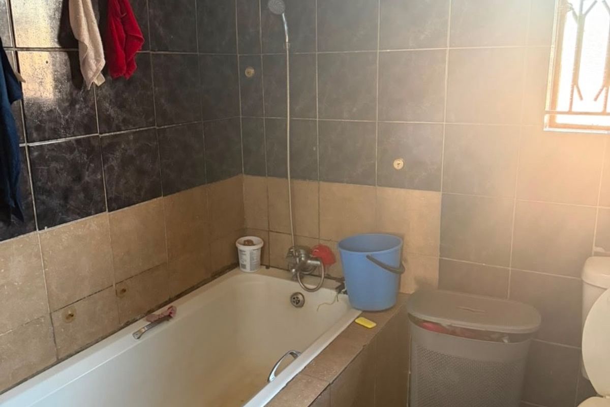 A dated bathroom featuring a built-in bathtub with shower mixer, ceramic tiling, and a standard toilet, requiring cosmetic updates and maintenance.