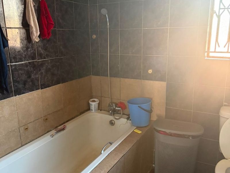 A dated bathroom featuring a built-in bathtub with shower mixer, ceramic tiling, and a standard toilet, requiring cosmetic updates and maintenance.