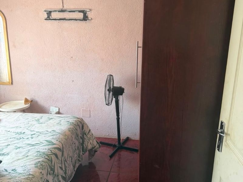 A bedroom featuring tiled flooring and a built-in wardrobe, currently showing signs of wear on the wall finishes.