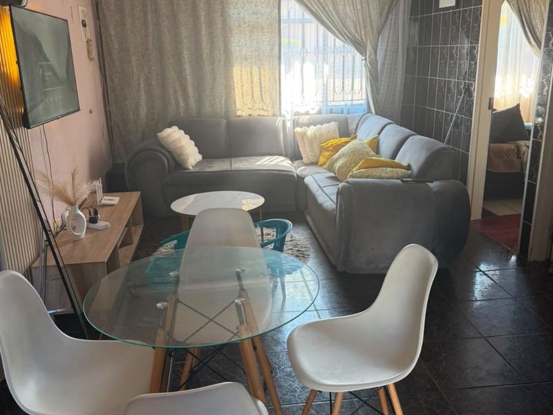 Open plan living and dining area featuring dark tiled flooring and a tiled feature wall, offering a compact layout for daily living.