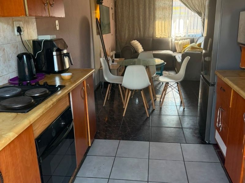 Open-plan kitchen and living area featuring built-in cabinetry, electric hob, oven, and tiled flooring, offering a functional layout for daily living.
