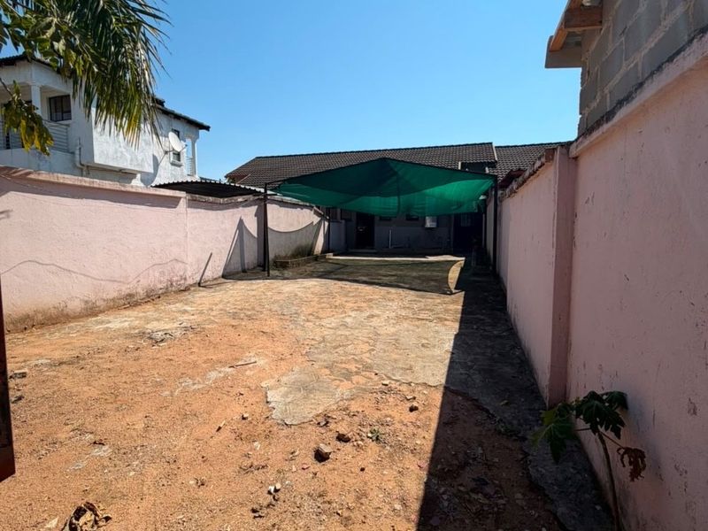 A rear outdoor area featuring perimeter boundary walls, a concrete paved section, and a shade cloth structure, requiring landscaping and surface maintenance.