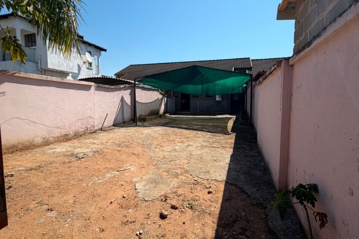 A rear outdoor area featuring perimeter boundary walls, a concrete paved section, and a shade cloth structure, requiring landscaping and surface maintenance.