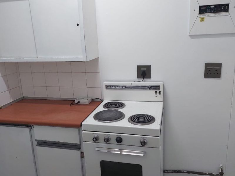 A compact kitchen area featuring basic cabinetry, a tiled backsplash, and a vintage electric stove with an integrated electrical distribution board.