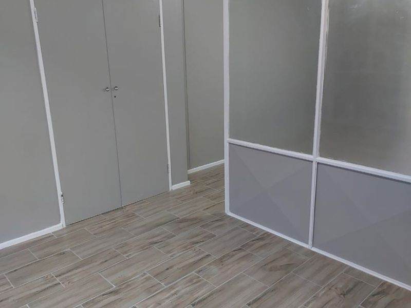 An empty bedroom featuring modern wood-look tiled flooring, built-in storage cupboards, and a contemporary glass and frame partition screen.