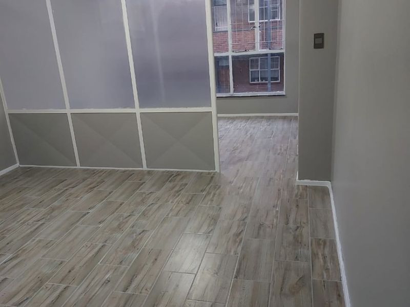 An empty living area featuring modern wood-look tile flooring and a semi-transparent partition wall, providing a clean and neutral space.