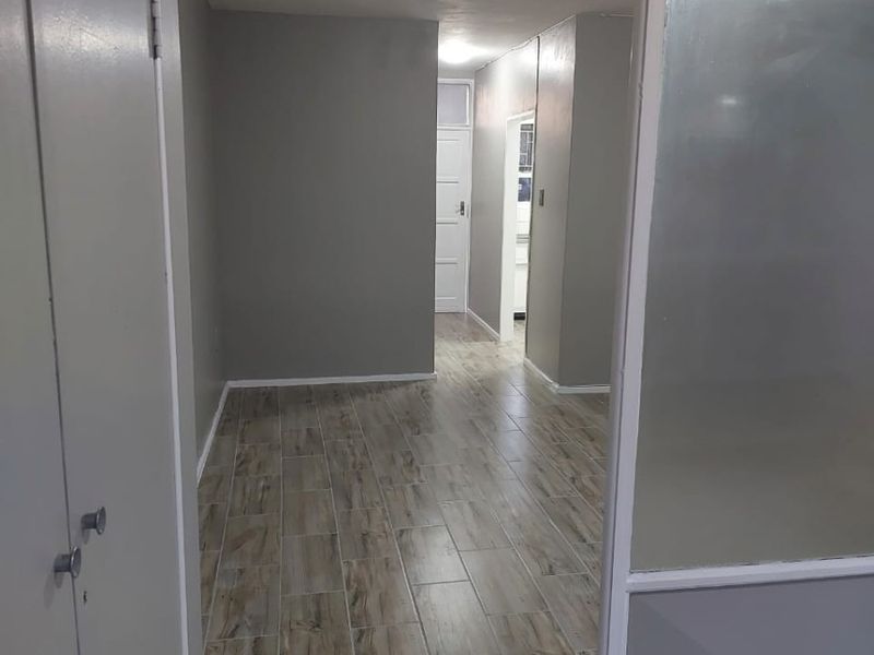 A clean, empty hallway featuring modern wood-look tile flooring, built-in storage cupboards, and a frosted glass partition wall.