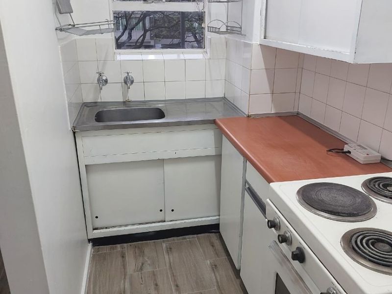 Compact kitchen featuring a stainless steel sink, electric stove, laminate countertops, and wood-look floor tiles with white tiled backsplash.