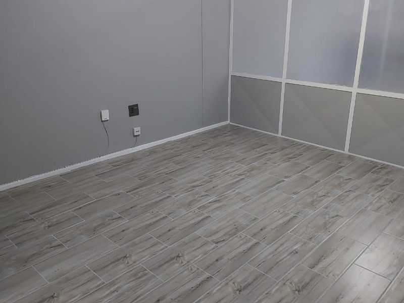 An empty living area featuring modern wood-look tile flooring and a contemporary frosted glass partition wall.