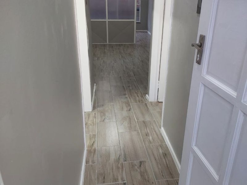A clean, empty hallway featuring modern wood-look floor tiles and neutral wall finishes, leading into an adjacent living space.