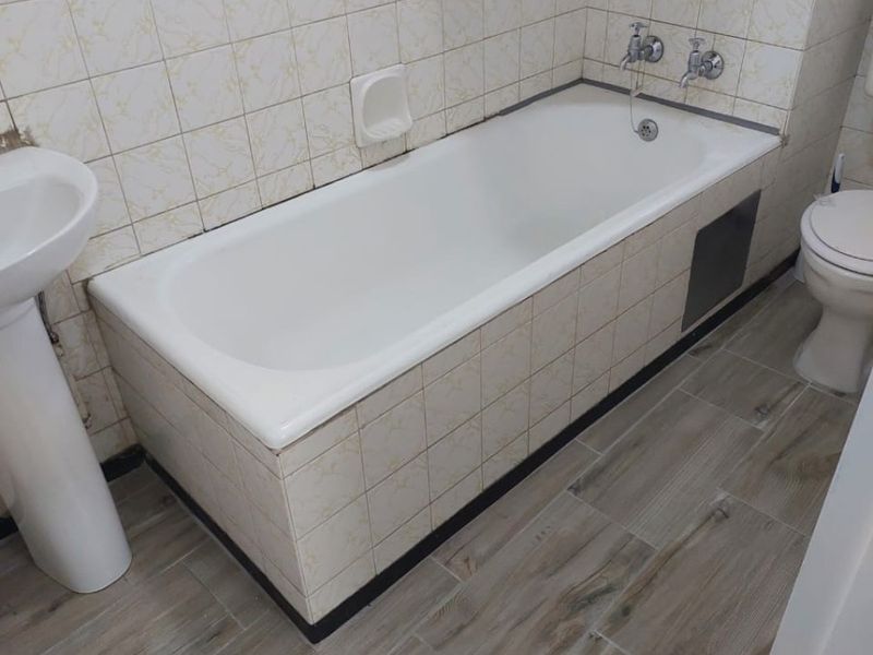 A functional bathroom featuring a bathtub, pedestal basin, and toilet with neutral wall tiling and wood-look floor tiles.
