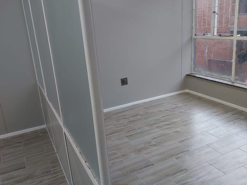 An empty bedroom featuring wood-look tile flooring, a frosted glass partition wall, and a large window with security bars.