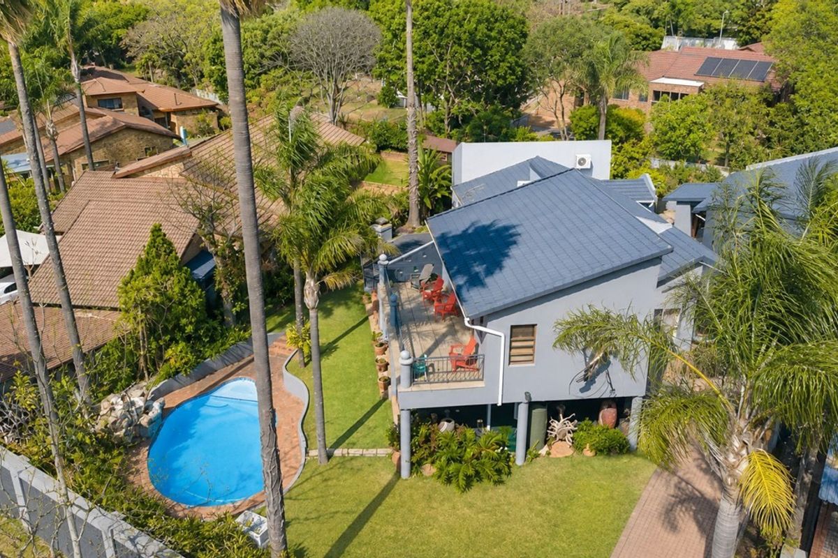 Aerial view of the property featuring a swimming pool, landscaped garden, and an elevated deck area with a tiled roof structure.